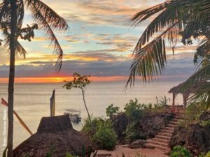 Sonnenuntergang über dem Meer auf Siquijor mit Palmen, Boot und tropischer Küstenlandschaft.