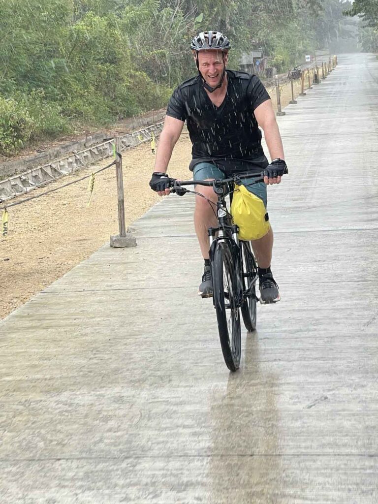 Radfahrer mit Helm fährt bei starkem Regen auf einer Straße auf der Insel Siquijor.