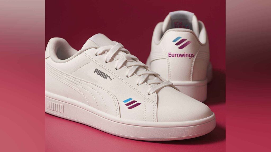 Weißer Puma-Sneaker mit Eurowings-Logo vor pinkfarbenem Hintergrund.