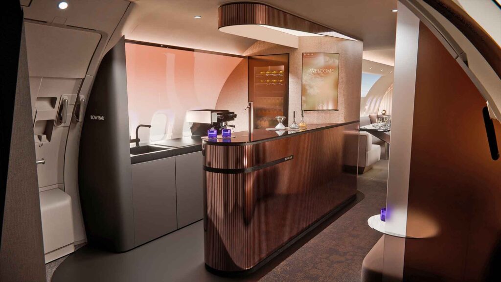 Innenansicht einer luxuriösen Flugzeugbar mit einer geschwungenen, kupferfarbenen Front. Im Hintergrund sind eine Kaffeemaschine, ein Spülbecken und ein digitaler „Welcome“-Bildschirm zu sehen.