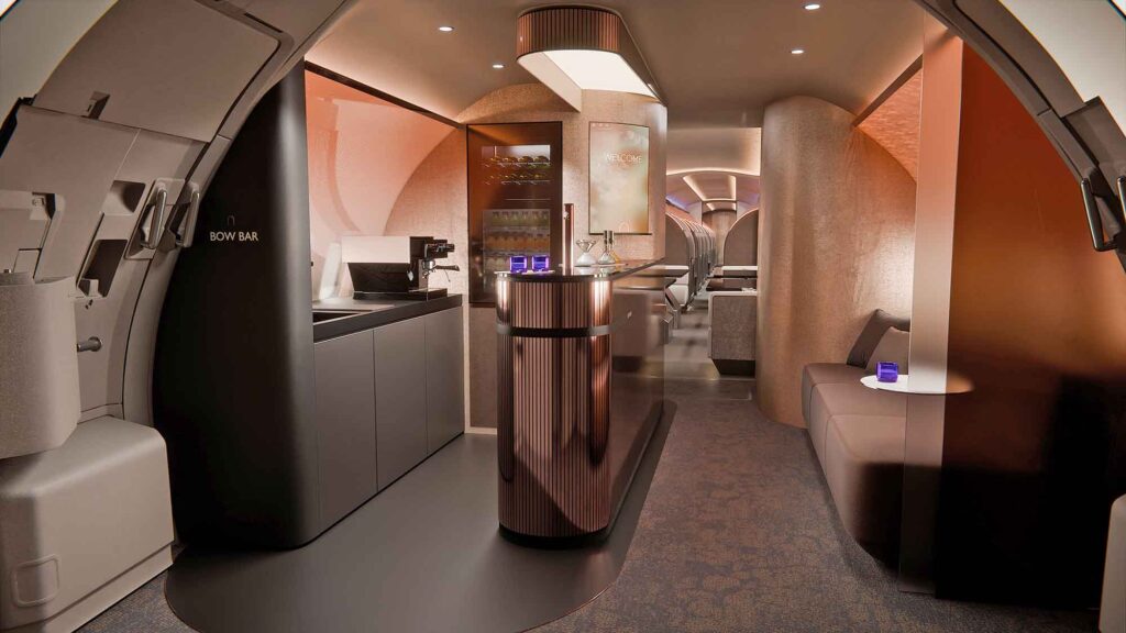 Eine Weitwinkelaufnahme des Eingangsbereichs im Flugzeug. Links befindet sich die kupferfarbene Bar, rechts eine gemütliche Sitzgelegenheit und im Hintergrund der Blick in den Gang der Kabine.