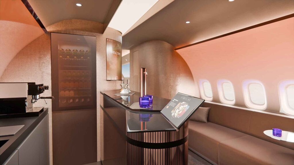 Nahaufnahme des Bar-Tresens. Auf der dunklen Oberfläche stehen ein Tablet mit Menüführung und blaue Gläser. Im Hintergrund sind die beleuchteten Flugzeugfenster und eine Couch zu erkennen.