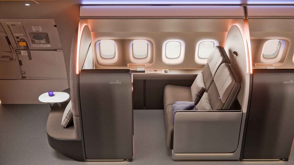 Seitenansicht einer privaten Flugzeug-Suite. Sie bietet ein breites Sofa mit Kissen, warme Ambientebeleuchtung an den geschwungenen Wänden und drei Fenster.