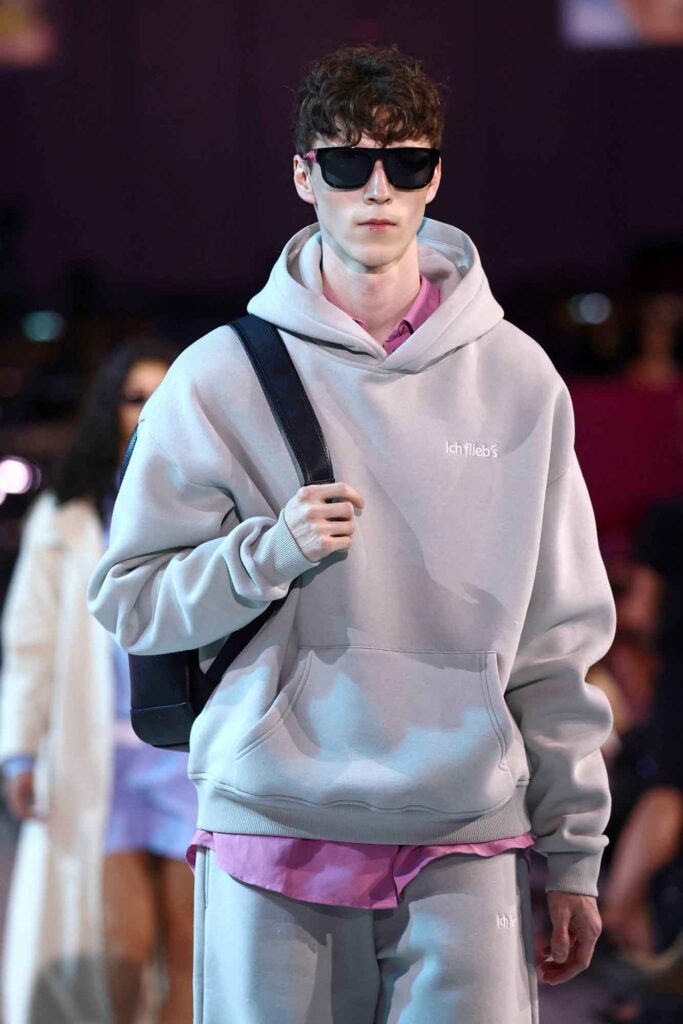 Eurowings: Was sonst noch wichtig ist 21 Männliches Model mit Sonnenbrille trägt grauen Hoodie und Rucksack bei einer Modenschau
