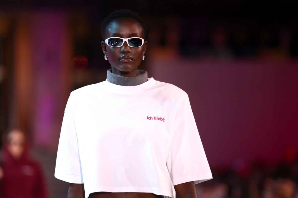 Eurowings: Was sonst noch wichtig ist 22 Model mit Sonnenbrille präsentiert weißes Crop-Shirt mit „Ich flieb’s“-Schriftzug auf einer Fashion-Show