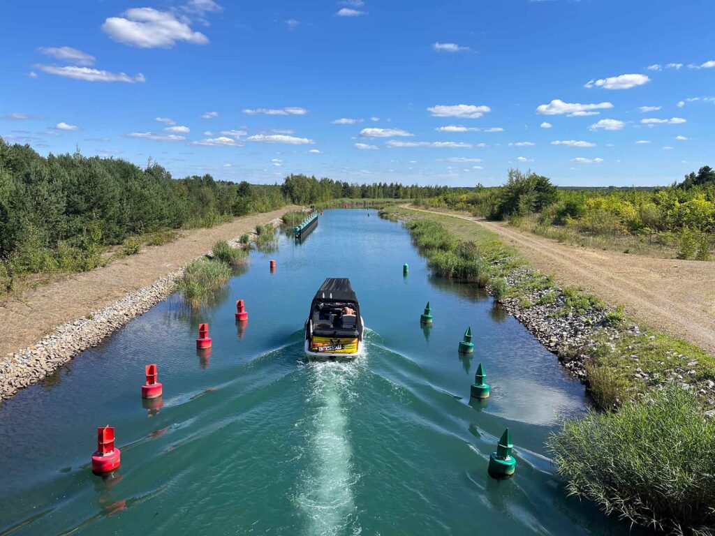 Lausitzer Seenland - Fünf-Seen-Verbund öffnet Ende Juni 7 Motorboot fährt durch den schmalen Barbara-Kanal, gesäumt von grünen Ufern und markiert durch rote und grüne Tonnen