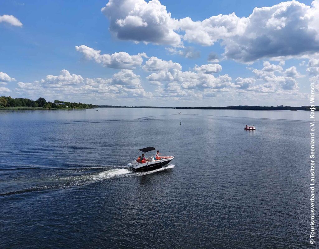 Motorboot und Tretboot sind auf dem offenen Wasser des Senftenberger Sees unterwegs unter einem Himmel mit vielen Wolken