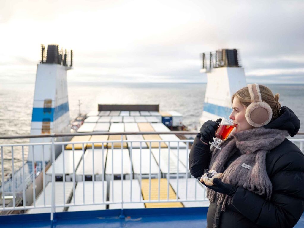 Passagierin mit warmer Kleidung genießt Tee an Deck einer Finnlines-Fähre mit Blick auf das Meer