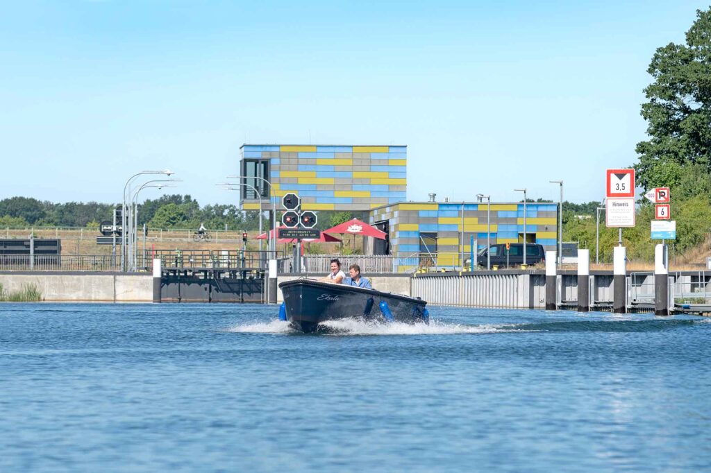 Lausitzer Seenland - Fünf-Seen-Verbund öffnet Ende Juni 3 Motorboot fährt von einer Schleusenanlage im Koschener Kanal weg, im Hintergrund moderne Gebäude und Signalanlagen