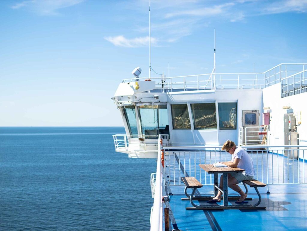 Passagier sitzt auf dem Außendeck einer Fähre und blickt auf ein Notizbuch