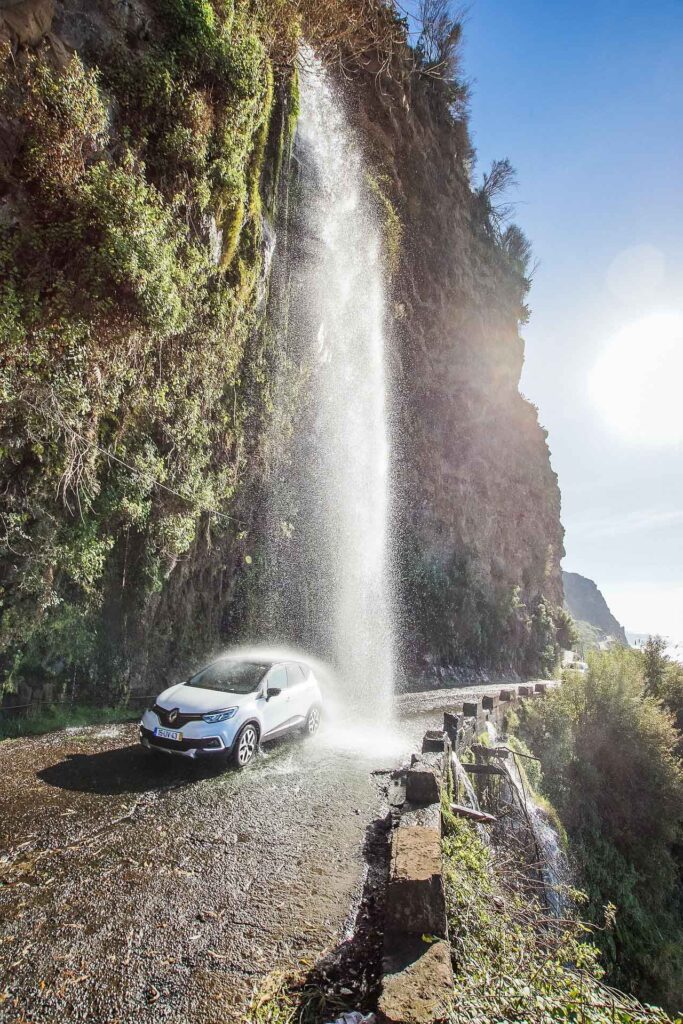 Madeira Aktivurlaub: Highlights für Wanderer, Abenteurer & Naturliebhaber 4 Auto fährt durch einen Wasserfall an einer Küstenstraße auf Madeira bei sonnigem Wetter