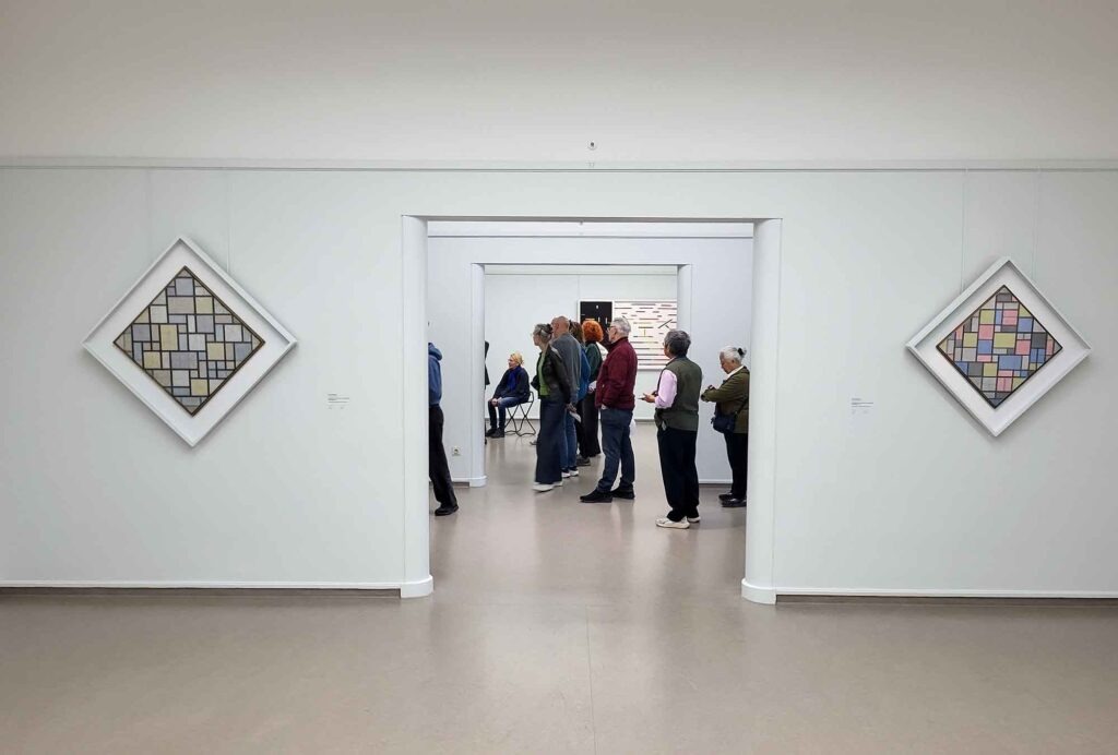 Blick durch einen Ausstellungsraum mit Besuchern und geometrischen Kunstwerken an den Wänden im Kröller-Müller Museum
