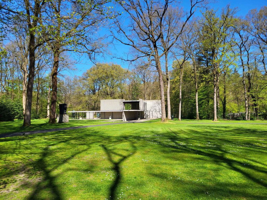 Pavillon inmitten einer weitläufigen Parklandschaft mit Rasenflächen und hohen Bäumen