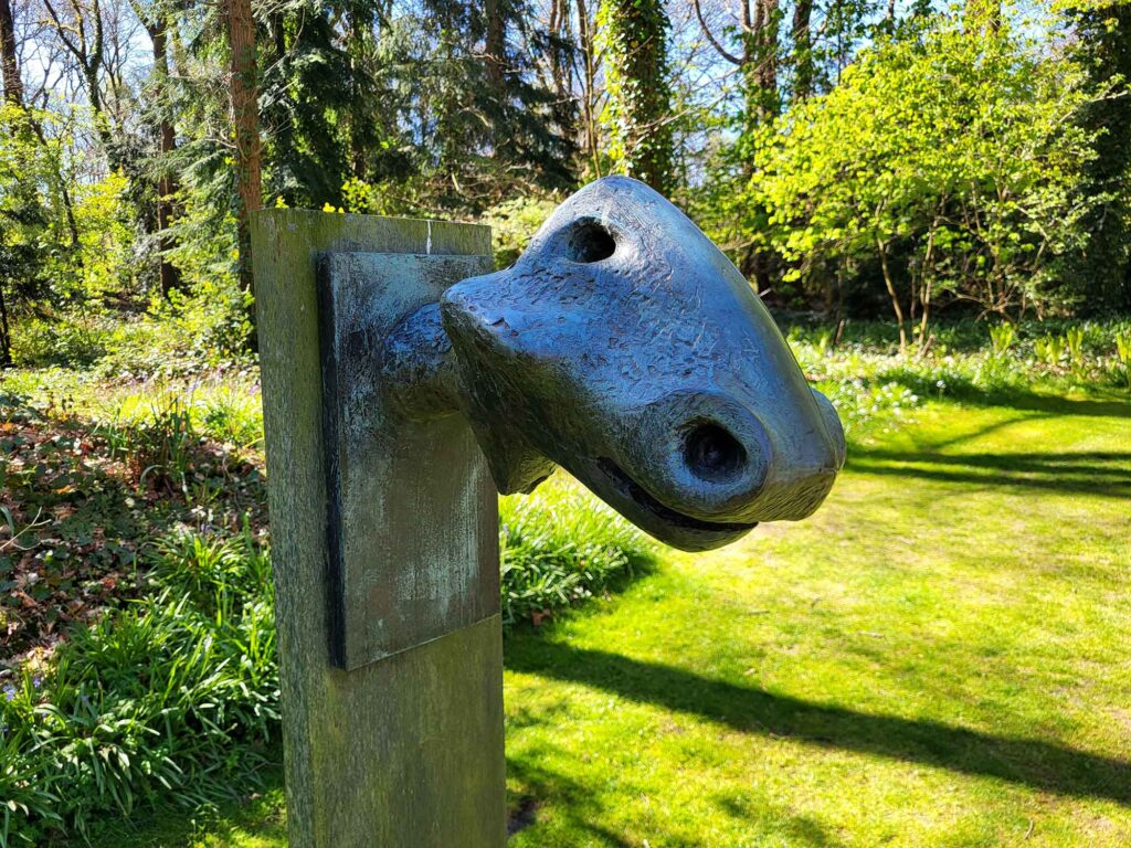 Detailaufnahme einer abstrakten Skulptur mit weichen Rundungen und Öffnungen vor grüner Natur