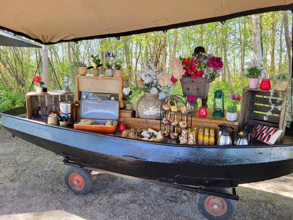 Maritimes Erbe erleben: Eine traditionelle Botterfahrt auf dem Veluwemeer ab Harderwijk 11 Ein als Buffetstation umgebautes schwarzes Boot auf Rädern unter einer Plane, dekoriert mit einem alten Röhrenradio, Blumen, Laternen und Kaffeekannen.