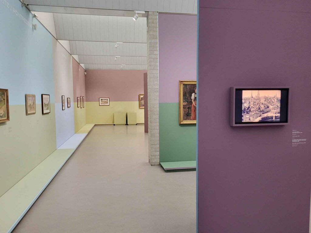 Moderner Museumsraum mit pastellfarbenen Wänden und mehreren gerahmten Gemälden entlang der Wände