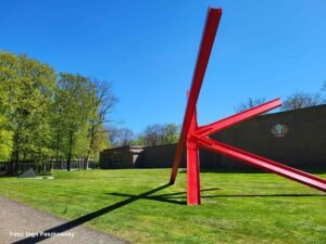 Große abstrakte rote Stahlskulptur auf einer Wiese vor dem modernen Museumsbau