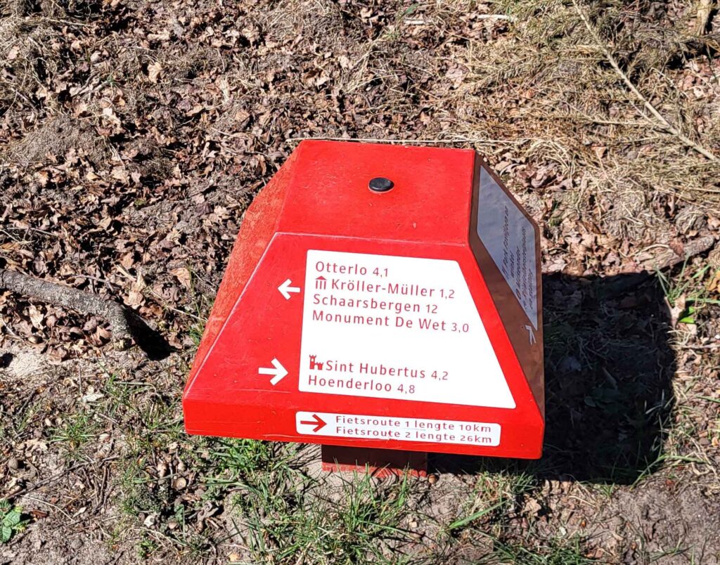 Roter Wegweiser mit Entfernungsangaben zu Orten im Nationalpark De Hoge Veluwe