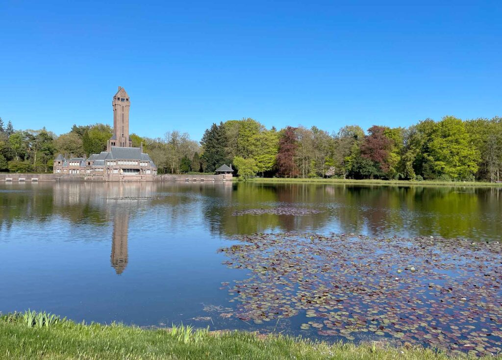 Jachthuis Sint Hubertus mit Turm spiegelt sich im Wasser eines Sees im Nationalpark De Hoge Veluwe