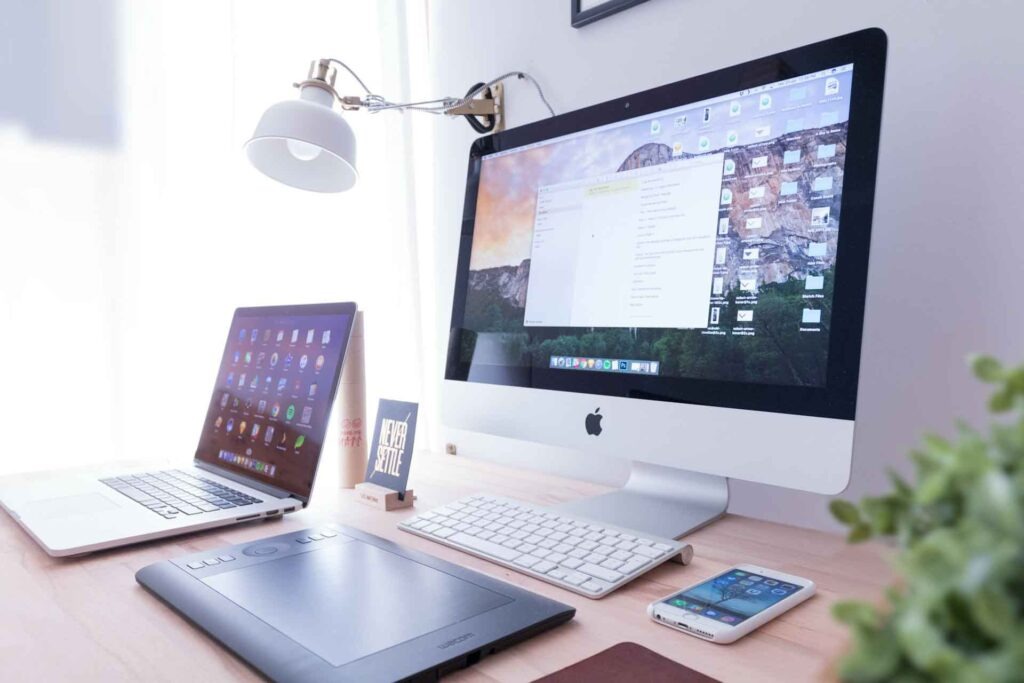 Silberner iMac, iPhone, McBook, Tablet von Wacom auf braunem Holztisch