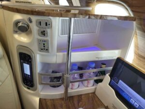 Detail eines Emirates-A380-Sitzplatzes mit Steckdosen, USB-Anschluss, Getränkefach und Bildschirm.