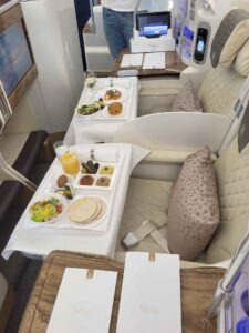 Emirates Business Class im Airbus A380 mit gedeckten Tischen, Speisen, Getränken und Menükarten.