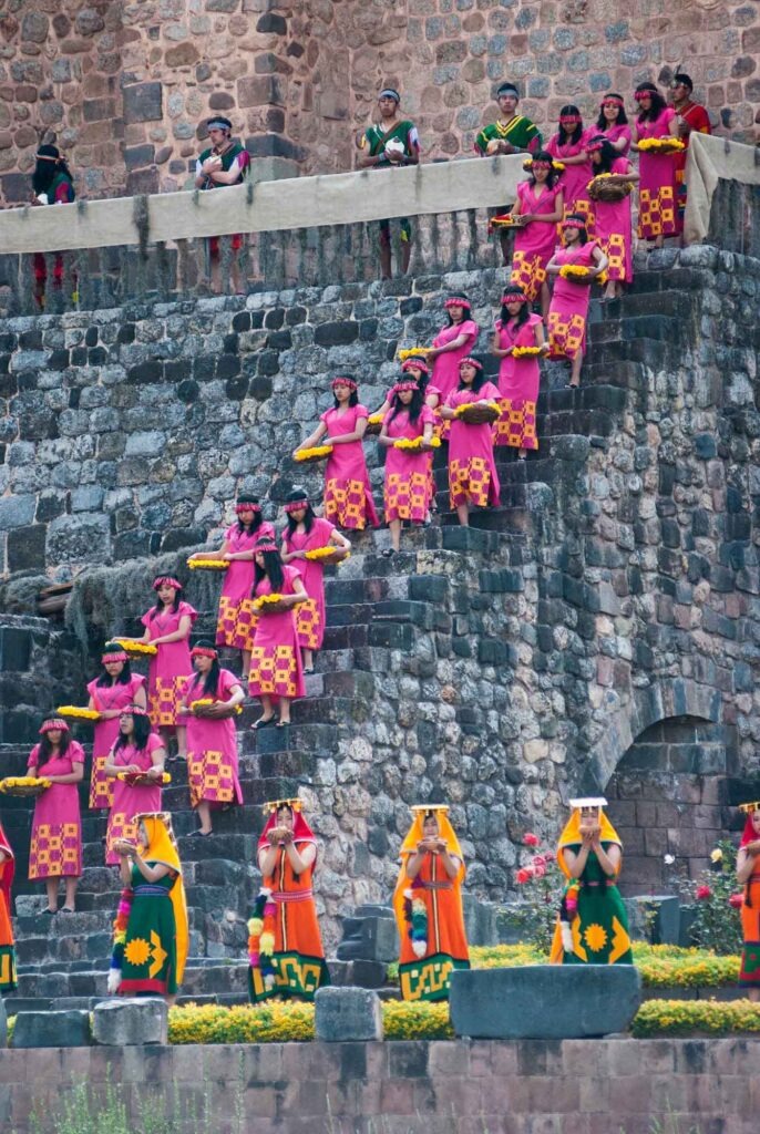 Inti Raymi: Cusco lässt das imperiale Erbe der Inka aufleben 3 Frauen in pinkfarbenen Gewändern tragen Blumen und Körbe auf Steintreppen während des Inti Raymi in Cusco.