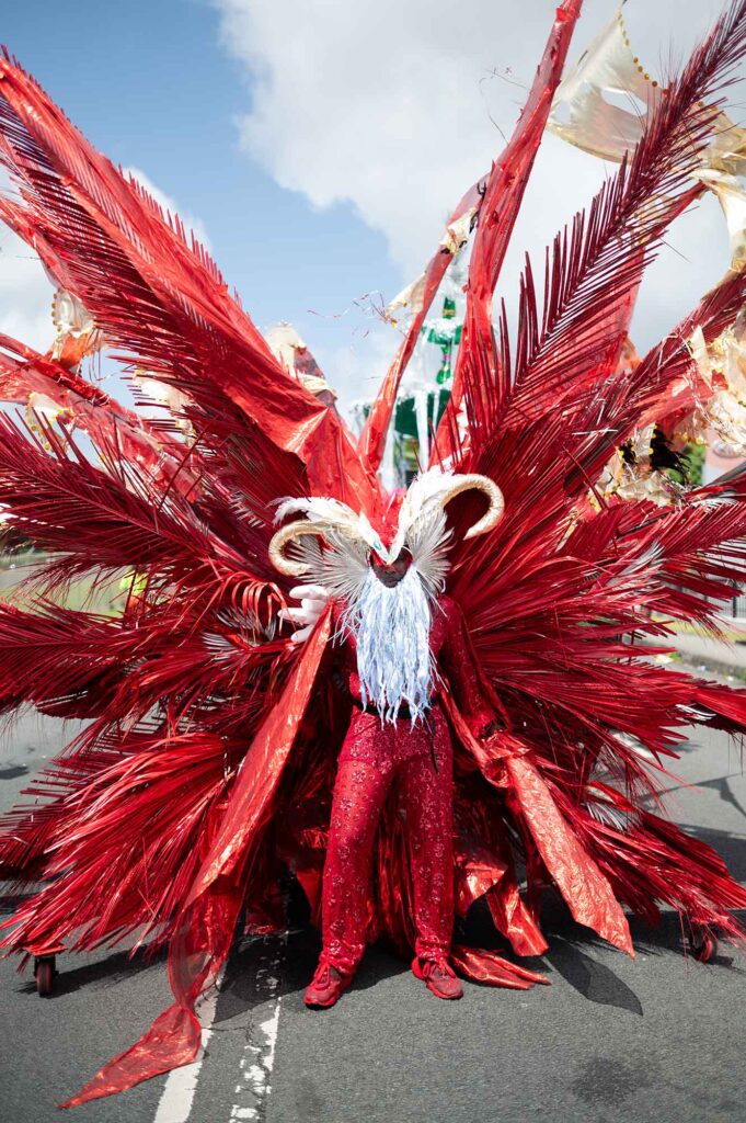 Teilnehmer der Parade of the Bands auf Saint Lucia in einem großen roten Karnevalskostüm mit Federn.
