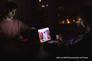 Zwei Personen sitzen nachts mit geöffneten Laptops in einem dunklen Raum.