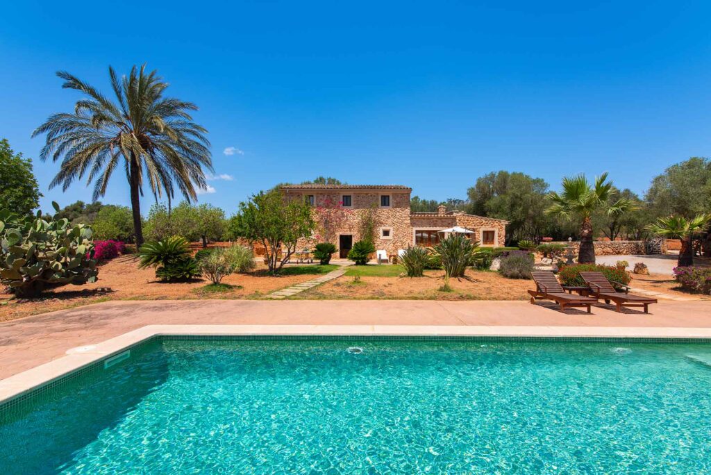 Fincaurlaub auf Mallorca: Worauf es ankommt 3 Finca Salva auf Mallorca mit großem Pool, Natursteinfassade, Palmen und mediterranem Garten