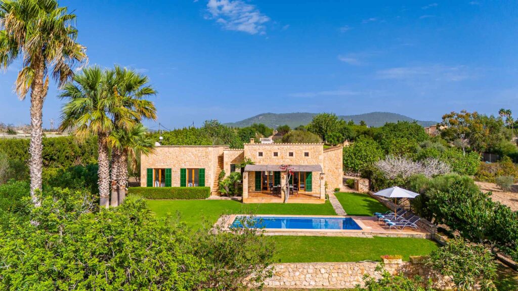 Fincaurlaub auf Mallorca: Worauf es ankommt 5 Natursteinhaus Casa Pula auf Mallorca mit privatem Pool, grünen Fensterläden, Palmen und gepflegtem Garten