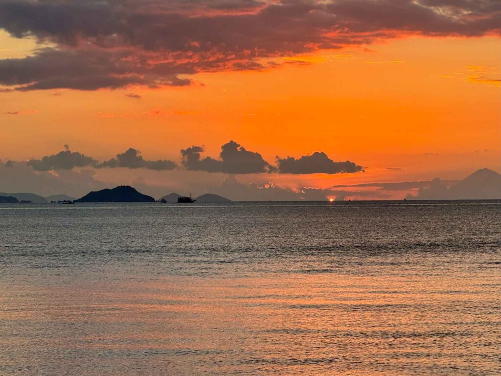Indonesien: Und dann steht der Komodowaran vor mir 11 Orangefarbener Sonnenuntergang über dem Meer mit dunklen Wolken und Inseln am Horizont