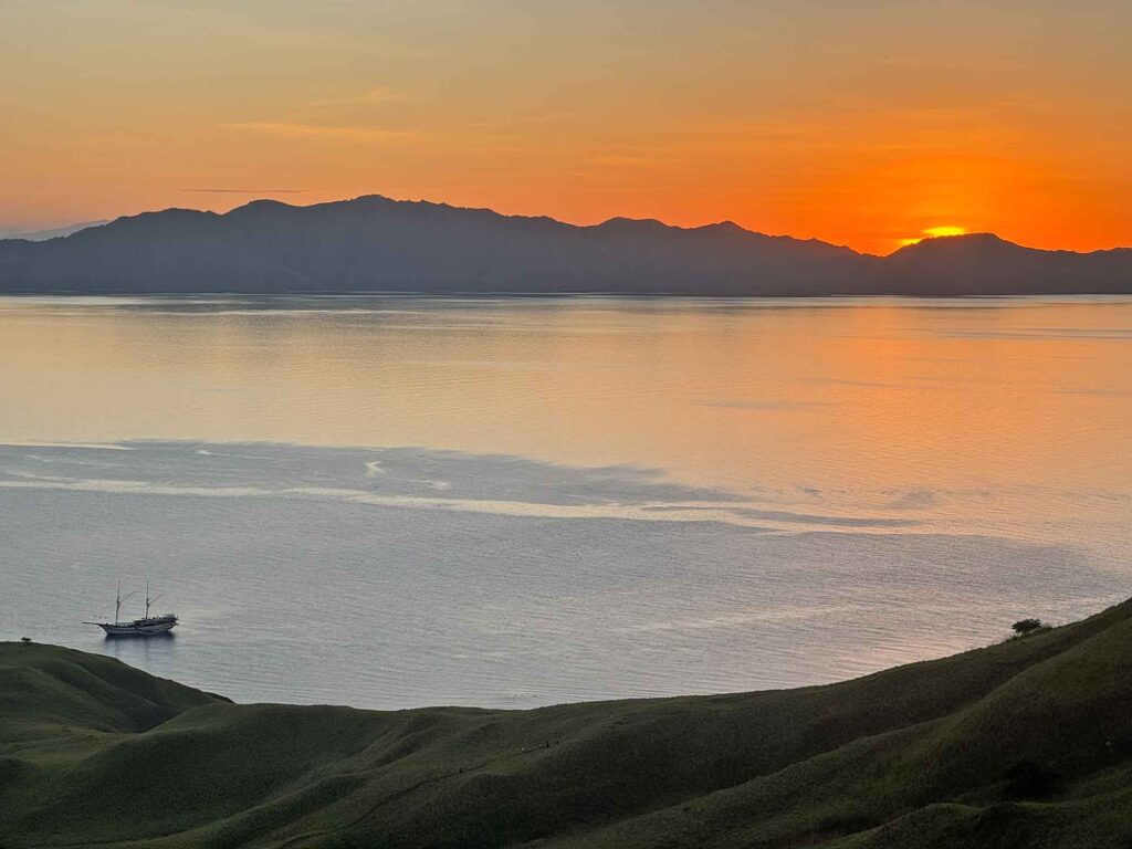 Indonesien: Und dann steht der Komodowaran vor mir 12 Sonnenuntergang hinter einer Bergsilhouette mit einem Segelboot auf dem ruhigen Meer