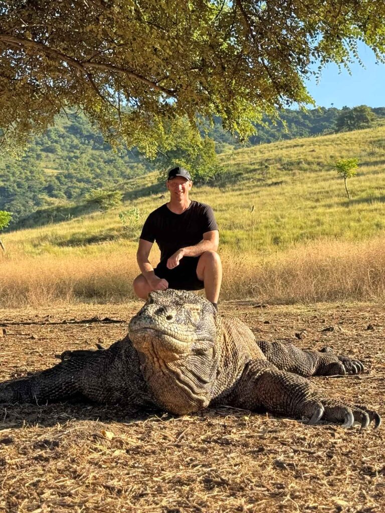 Indonesien: Und dann steht der Komodowaran vor mir 3 Thomas Bauer hinter einem großen Komodowaran in einer trockenen hügeligen Graslandschaft