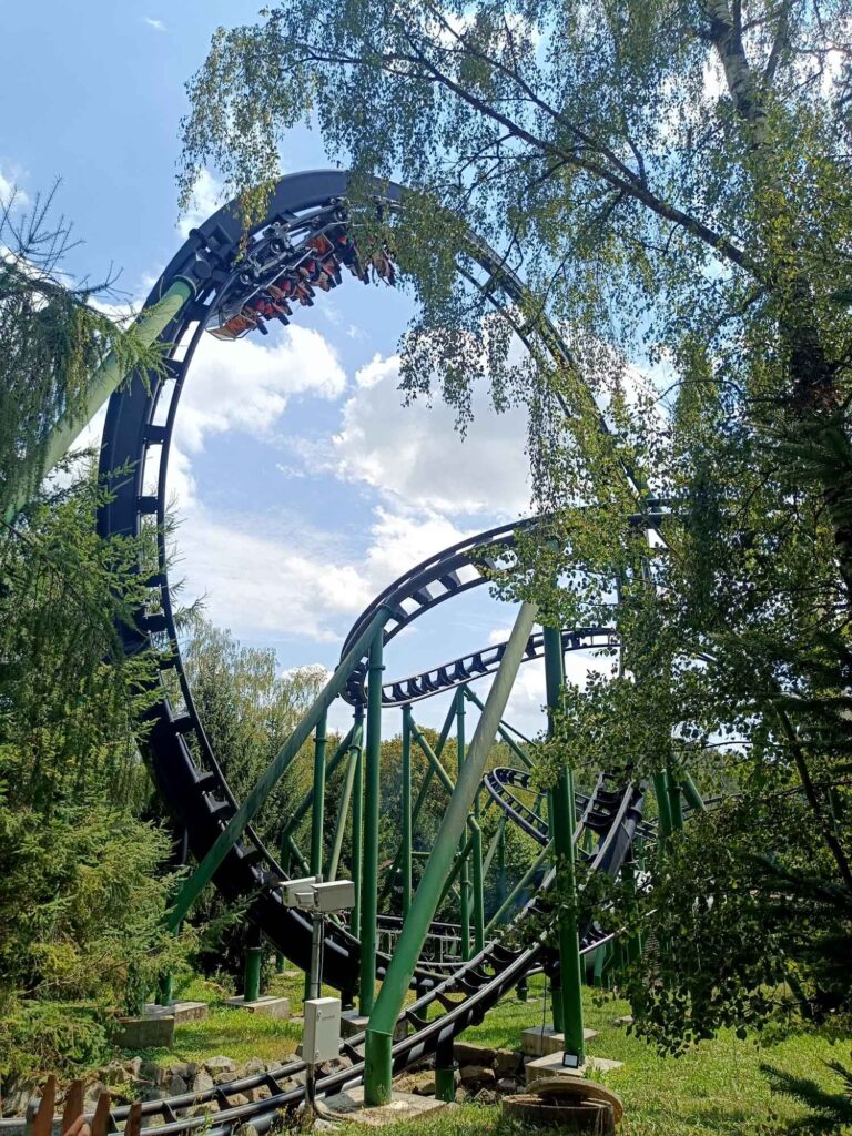 Ein Sommertag im Bayern-Park: Wasserspaß, Achterbahnen und Geduld beim Anstehen 5 Achterbahn Freischütz mit Fahrgästen in einem Überschlag zwischen Bäumen im Bayern-Park