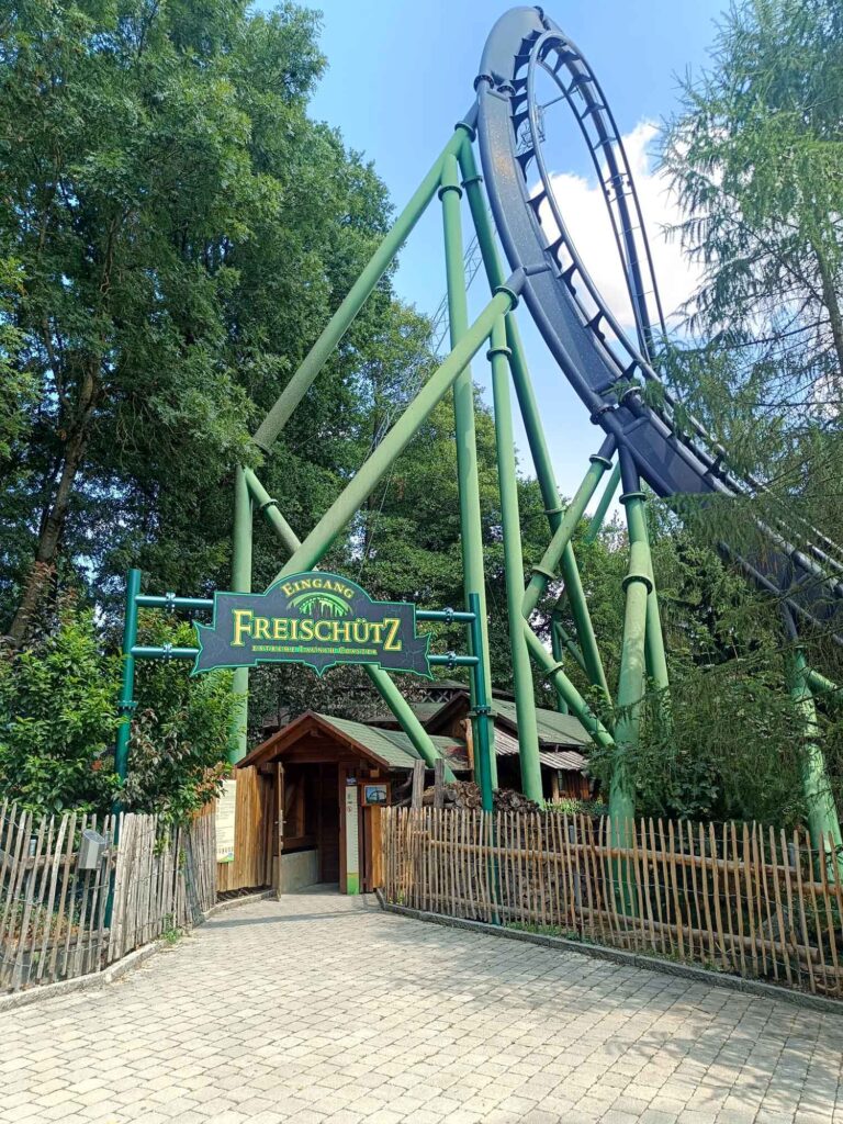 Ein Sommertag im Bayern-Park: Wasserspaß, Achterbahnen und Geduld beim Anstehen 4 Eingang zur Achterbahn Freischütz mit hoher schwarzer Schiene und grünen Stützen