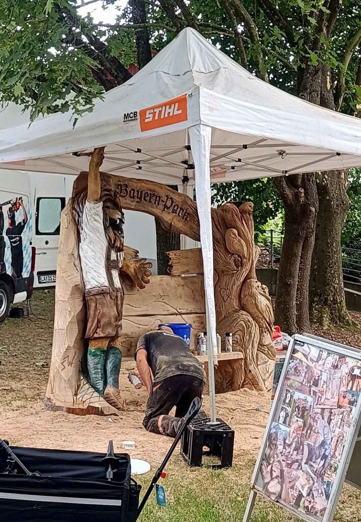 Ein Sommertag im Bayern-Park: Wasserspaß, Achterbahnen und Geduld beim Anstehen 14 Künstler bei der Arbeit an einer geschnitzten Holzskulptur unter einem Zelt