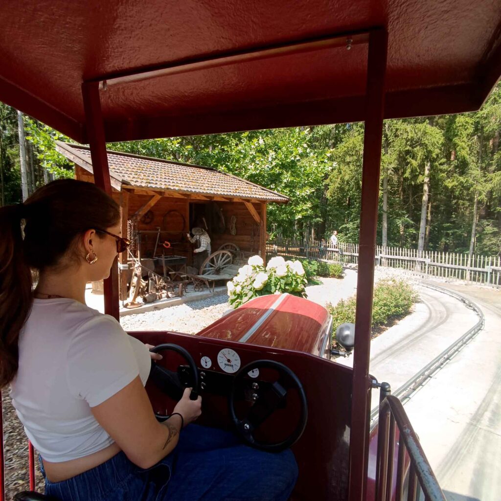 Ein Sommertag im Bayern-Park: Wasserspaß, Achterbahnen und Geduld beim Anstehen 11 Junge Frau am Steuer eines roten Oldtimer-Fahrzeugs auf einer Fahrattraktion im Bayern-Park