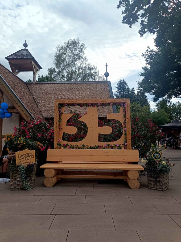 Ein Sommertag im Bayern-Park: Wasserspaß, Achterbahnen und Geduld beim Anstehen 16 Holzbank vor einer großen mit Blumen geschmückten Zahl 35 im Bayern-Park