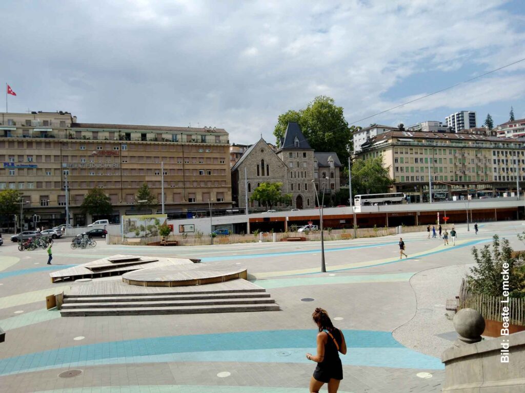 Was der Stern bedeutet 1 Großer gepflasterter und asphaltierter Platz in Lausanne mit Gebäuden und einer Kirche im Hintergrund.