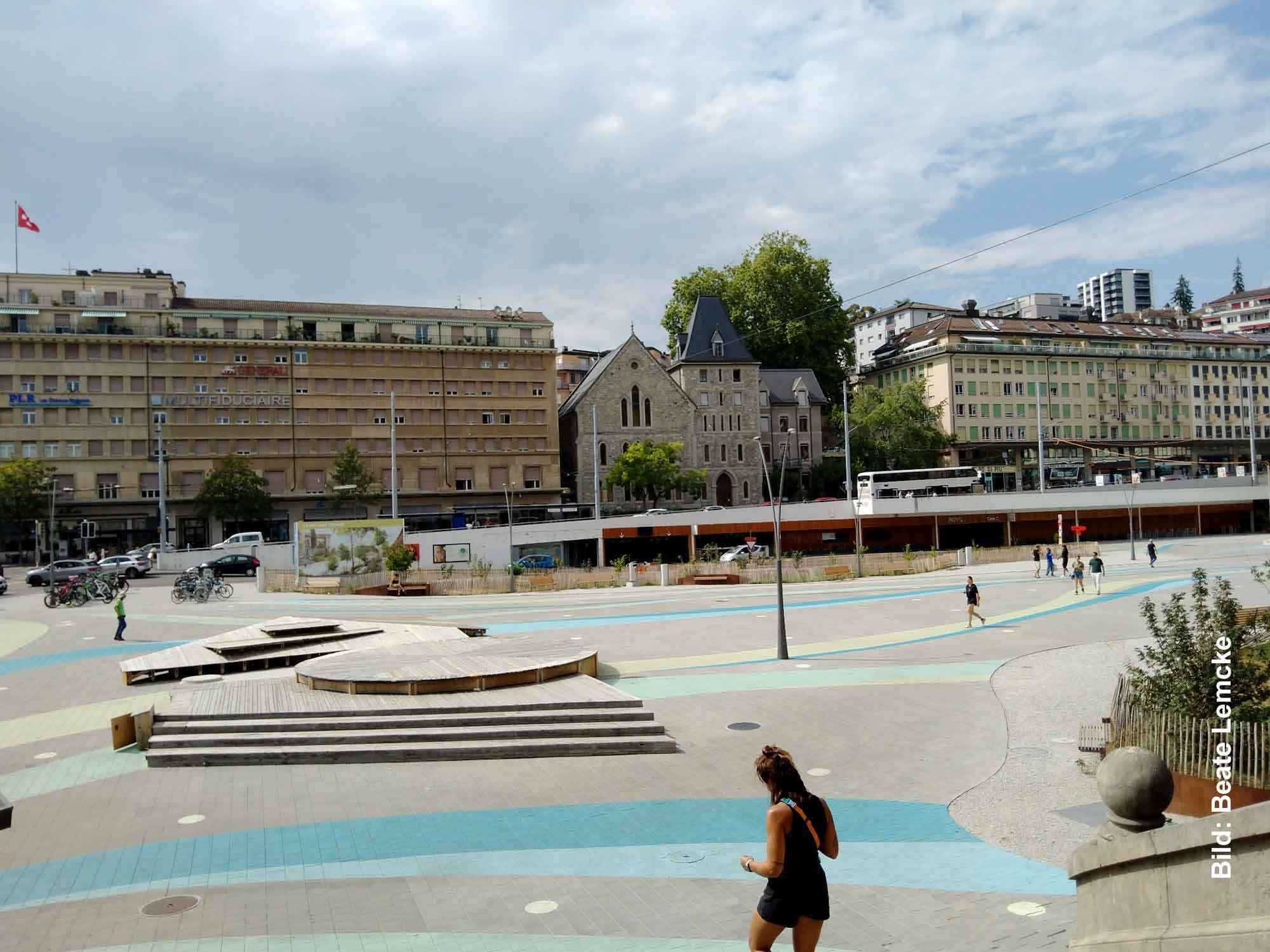 Radsport, Hitze und Erbauung 1 Großer gepflasterter und asphaltierter Platz in Lausanne mit Gebäuden und einer Kirche im Hintergrund.