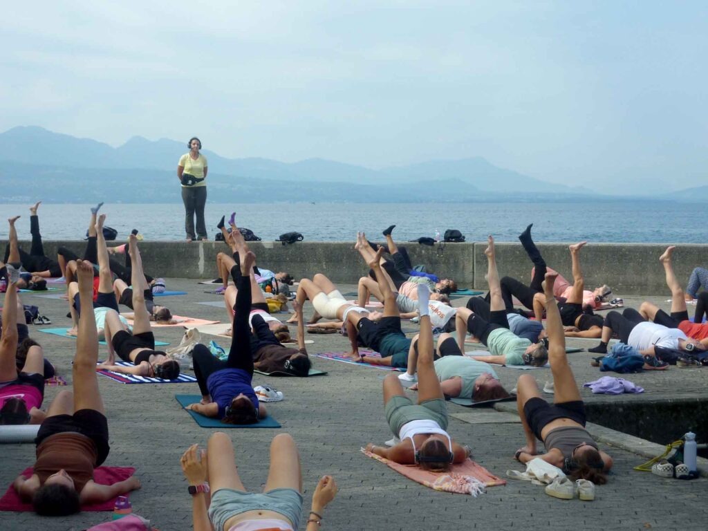 Radsport, Hitze und Erbauung 4 Sportgruppe bei Gymnastik auf Matten an der Uferpromenade von Lausanne mit Genfersee und Bergen.