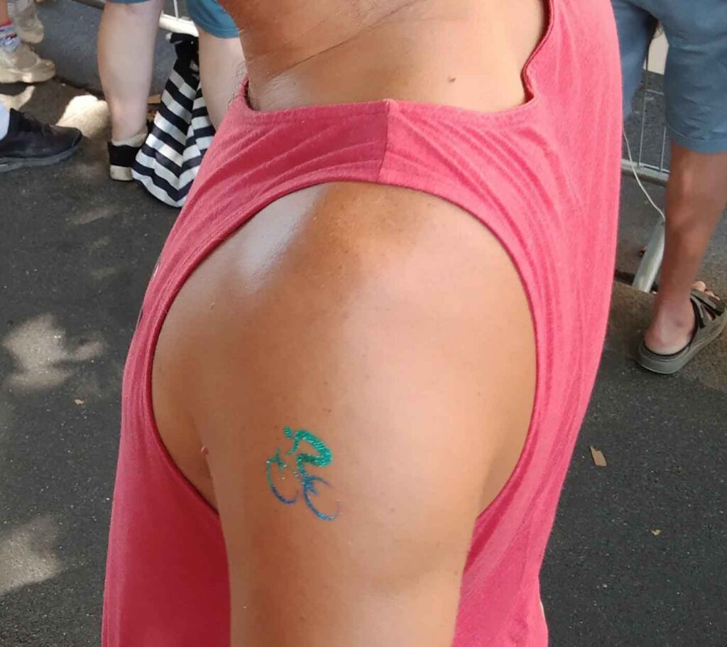Radsport, Hitze und Erbauung 7 Nahaufnahme eines Oberarms mit kNahaufnahme eines Oberarms mit einem temporären türkis-blauen Glitzer-Tattoo in Form eines Fahrrads.