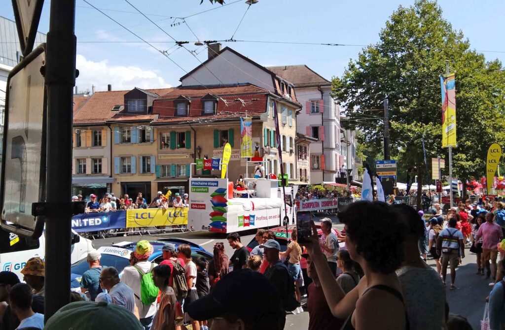 Werbewagen von ibis fährt vor dicht gedrängten Zuschauern durch eine Straße in Lausanne.
