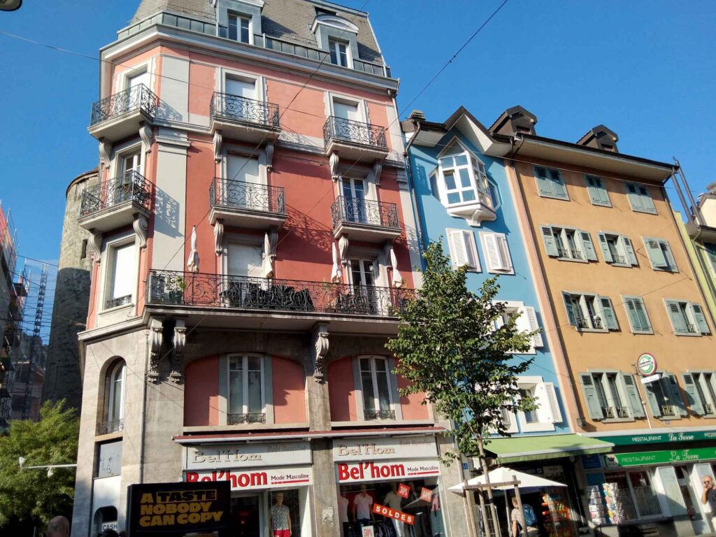 Farbenfrohe Altstadthäuser in Lausanne mit rosafarbener, blauer und ockerfarbener Fassade, Balkonen, Erker und Fensterläden.