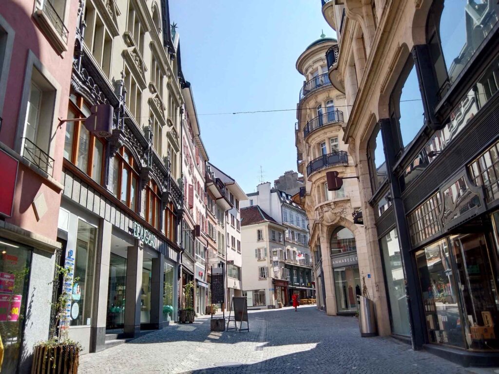 Ansteigende gepflasterte Einkaufsstraße in der Lausanner Altstadt mit historischen Fassaden, Schaufenstern und wenigen Passanten.