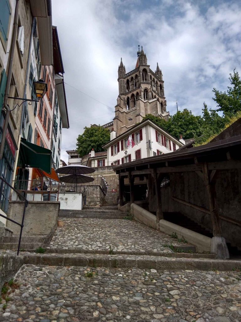 Radsport, Hitze und Erbauung 16 Steile gepflasterte Escaliers du Marché mit überdachter Holztreppe und dem Turm der Kathedrale von Lausanne im Hintergrund.