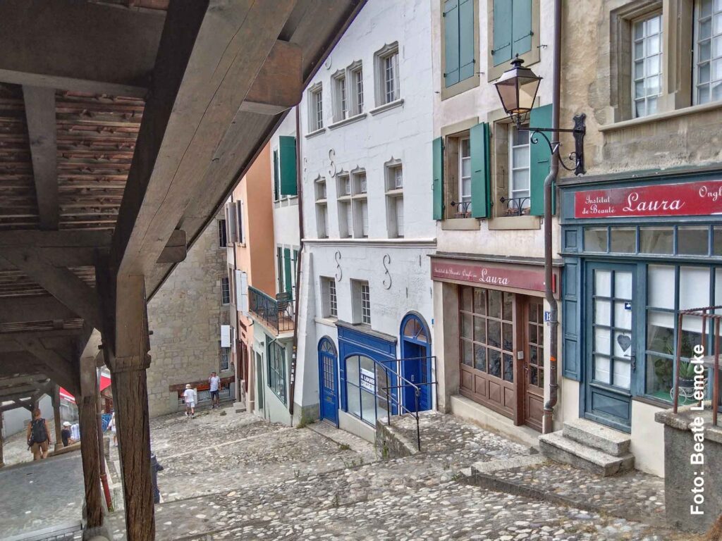 Blick unter die überdachte Holztreppe der Escaliers du Marché auf historische Häuser und eine steile Gasse in Lausanne.