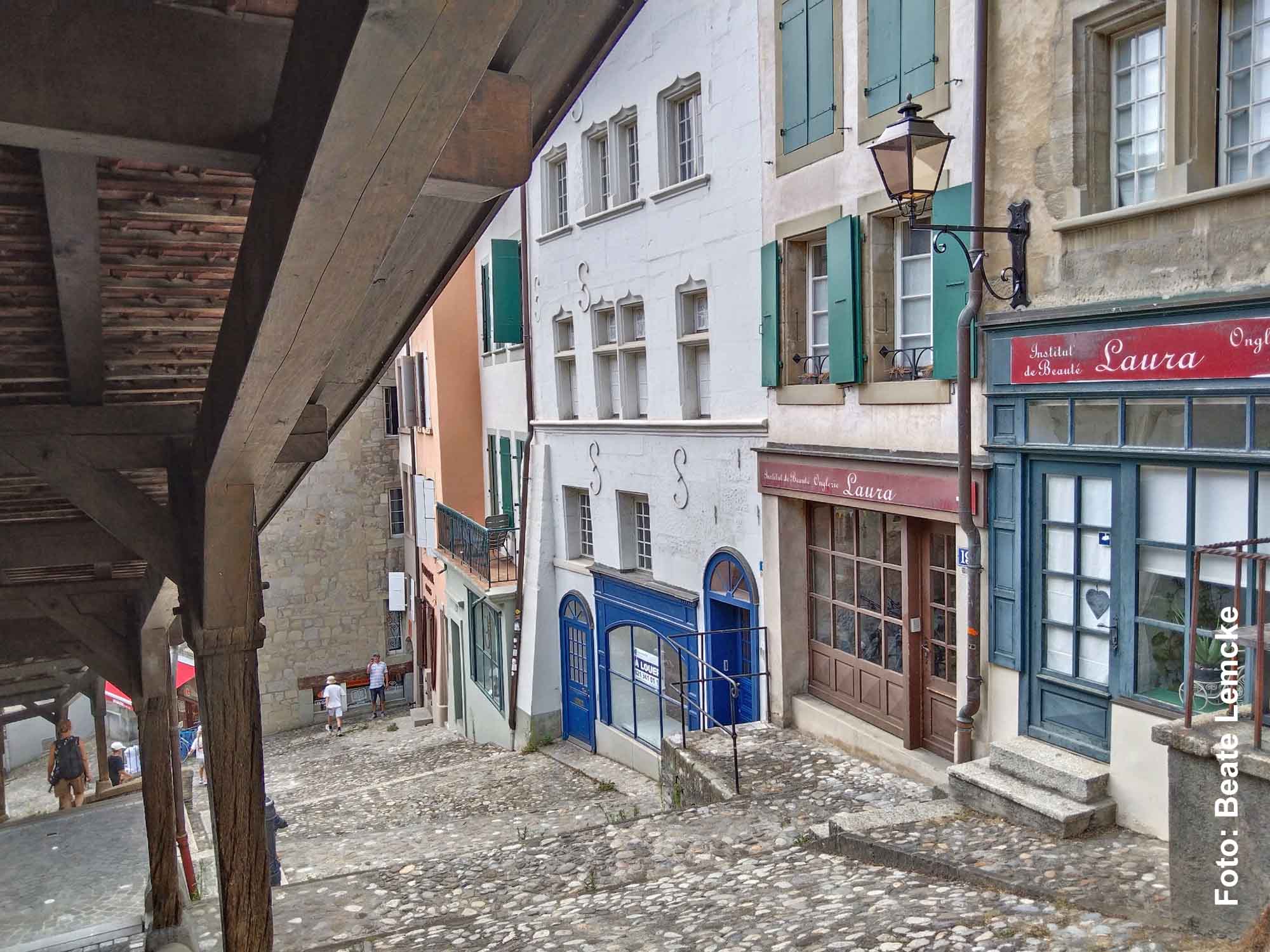 Blick unter die überdachte Holztreppe der Escaliers du Marché auf historische Häuser und eine steile Gasse in Lausanne.