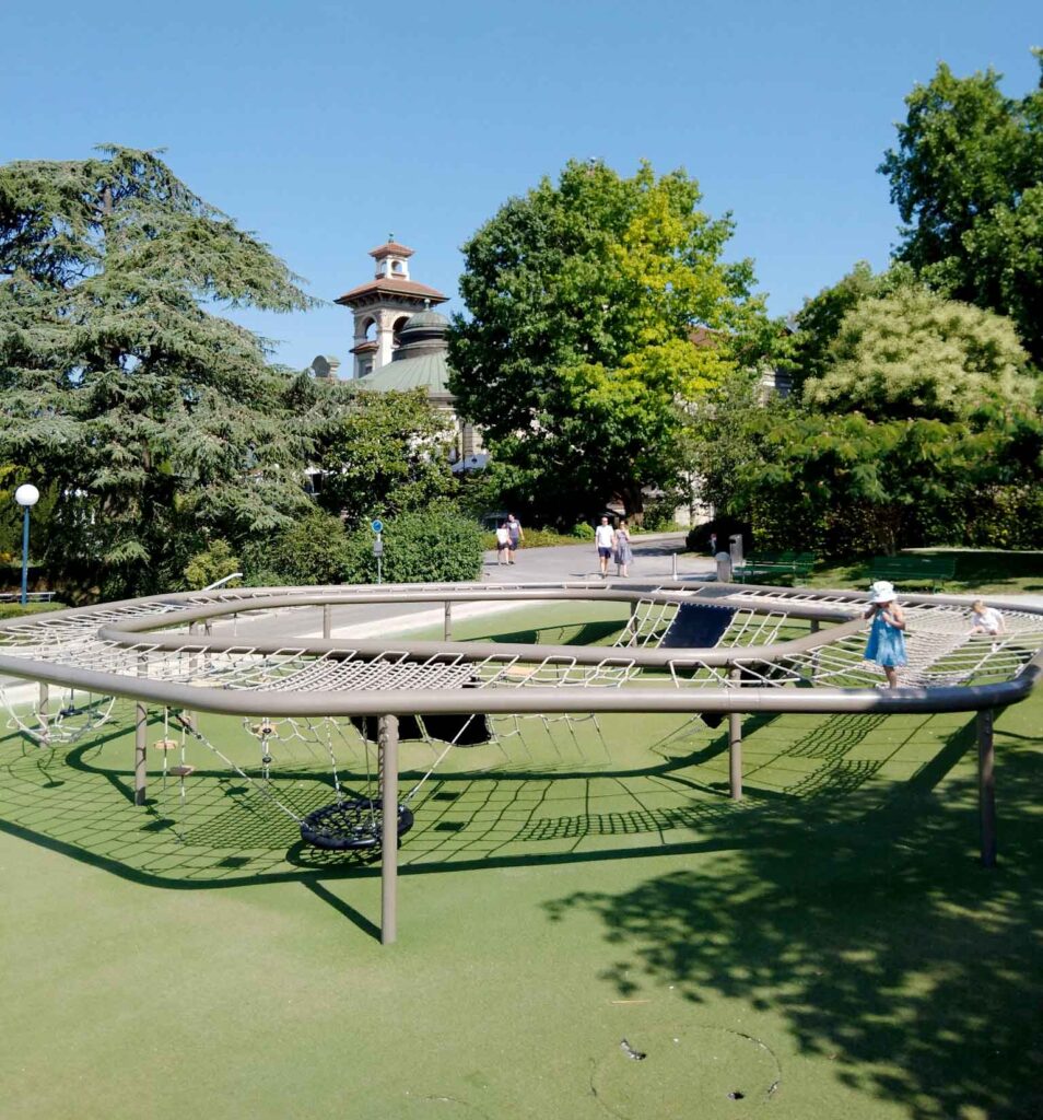 Großes rundes Klettergerüst mit Netzen und Schaukeln auf einem Spielplatz in der Esplanade de Montbenon in Lausanne.